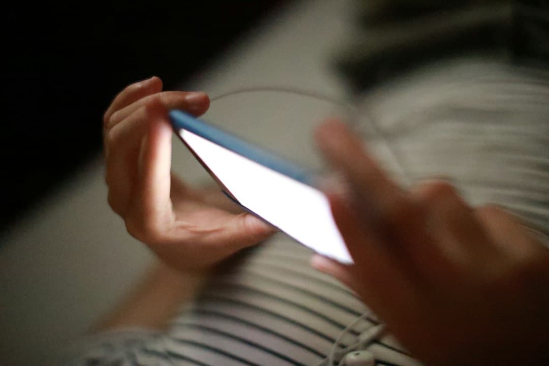 Une personne fait défiler l'écran d'un smartphone dans la pénombre, comme avec l'application Xenon IPTV